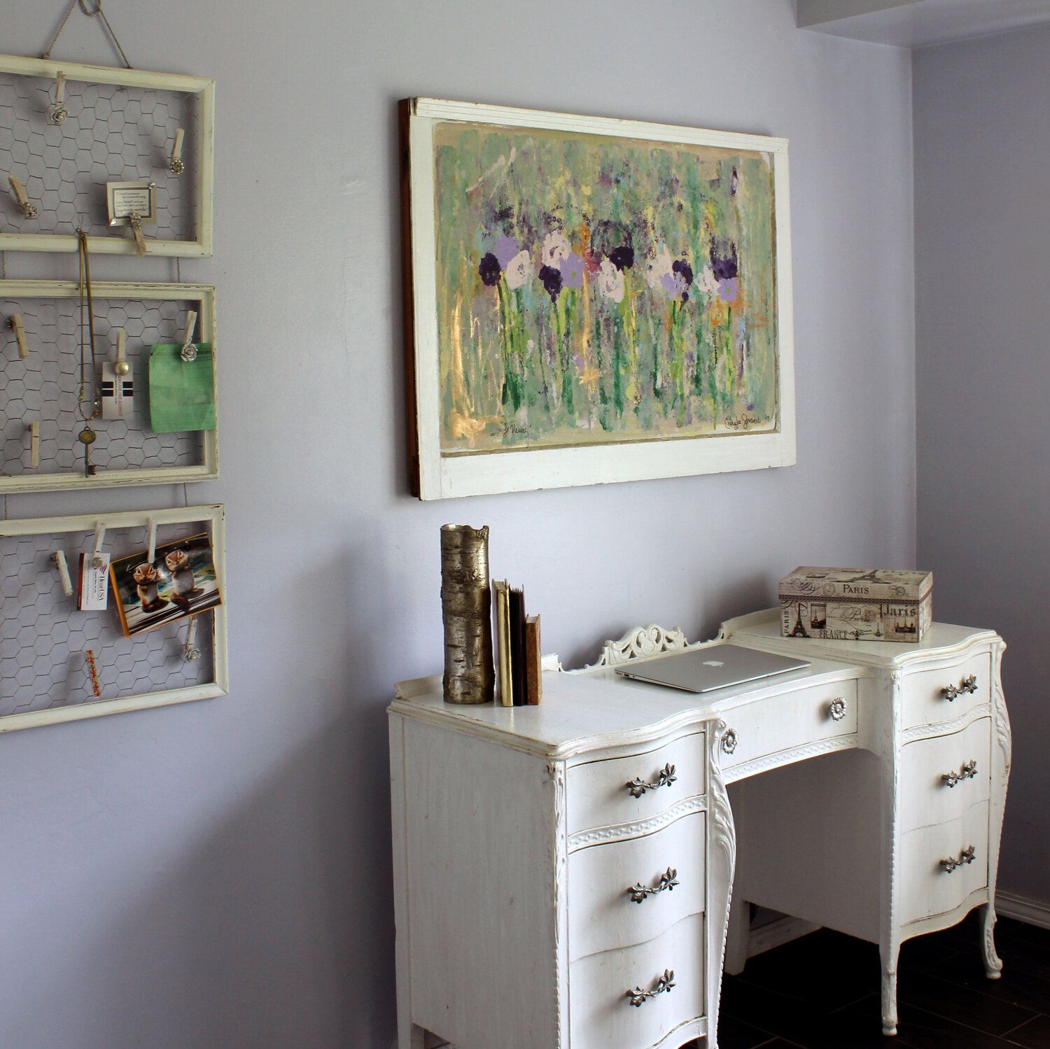 A white desk with a laptop and a painting on the wall above it