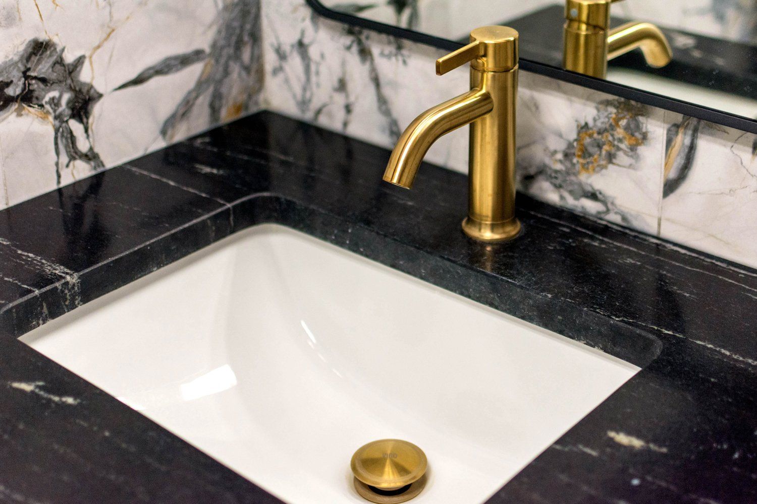 A bathroom sink with a gold faucet and a mirror.