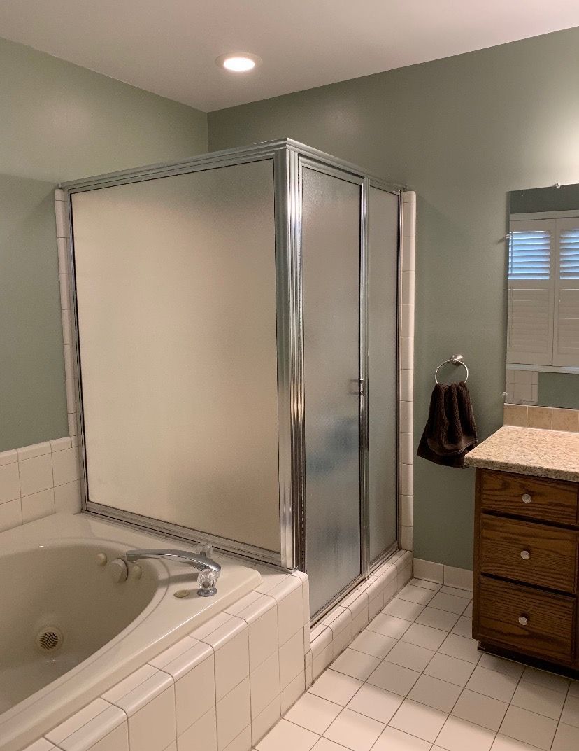 A bathroom featuring a white tiled bathtub, a glass-enclosed shower with a silver frame, and a wooden vanity cabinet.