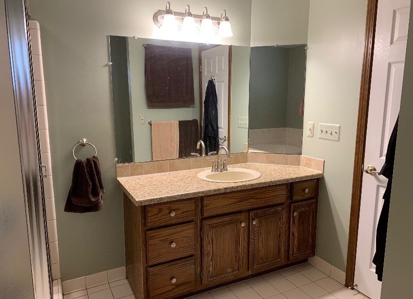 A bathroom vanity with a speckled countertop, wooden cabinets, a sink, and a large mirror against sage green walls.
