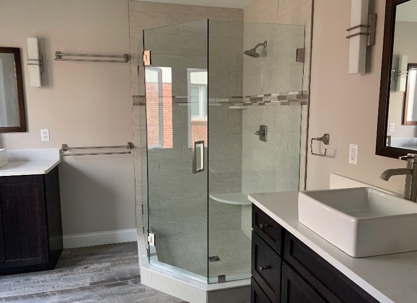 Modern bathroom with dark wood cabinets, a glass corner shower, and a white vessel sink on a white countertop.