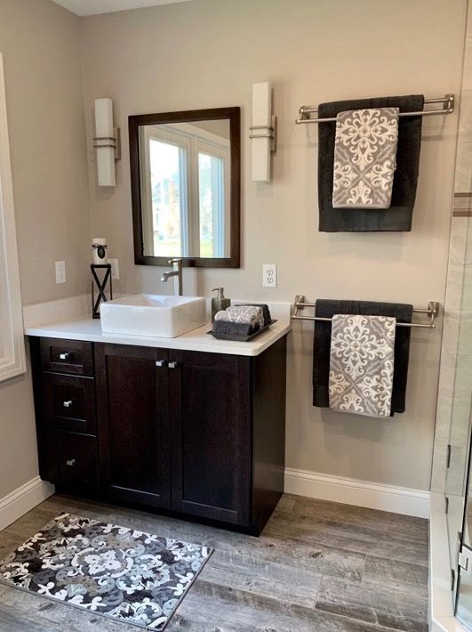 A modern bathroom with a dark wood vanity, white vessel sink, rectangular mirror, and gray patterned towels on towel bars.