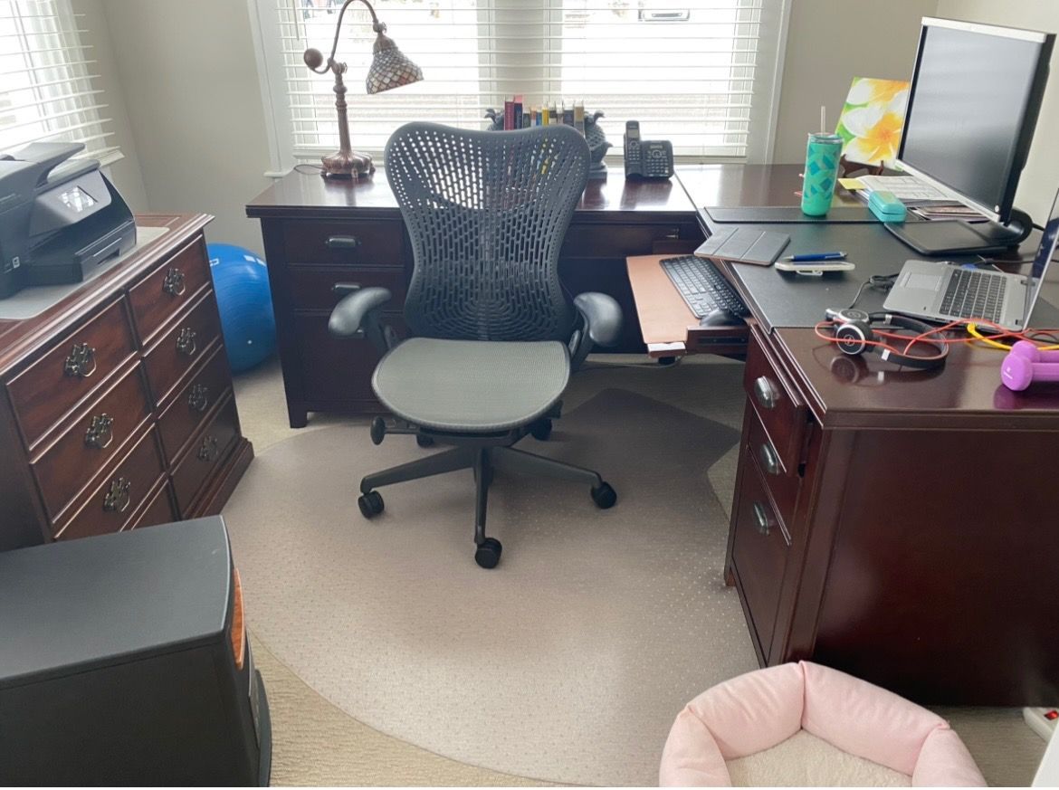A home office with a dark wood desk, an ergonomic black office chair, a computer monitor, a printer, and a pet bed.