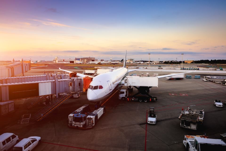 Airplane at airport gate with service vehicles; sunset.