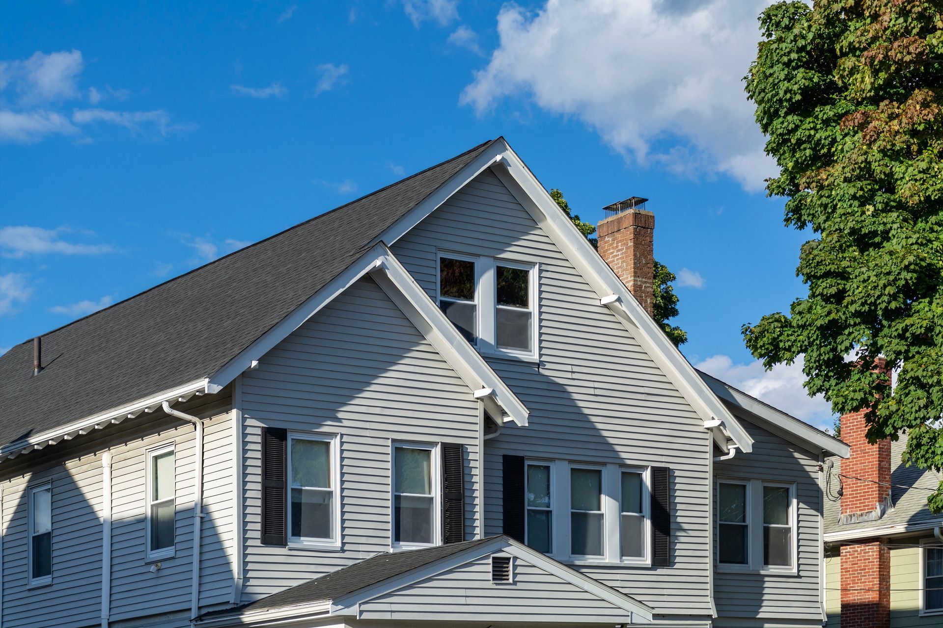 Gray house with white trim and dormers under a blue sky, viewed from below