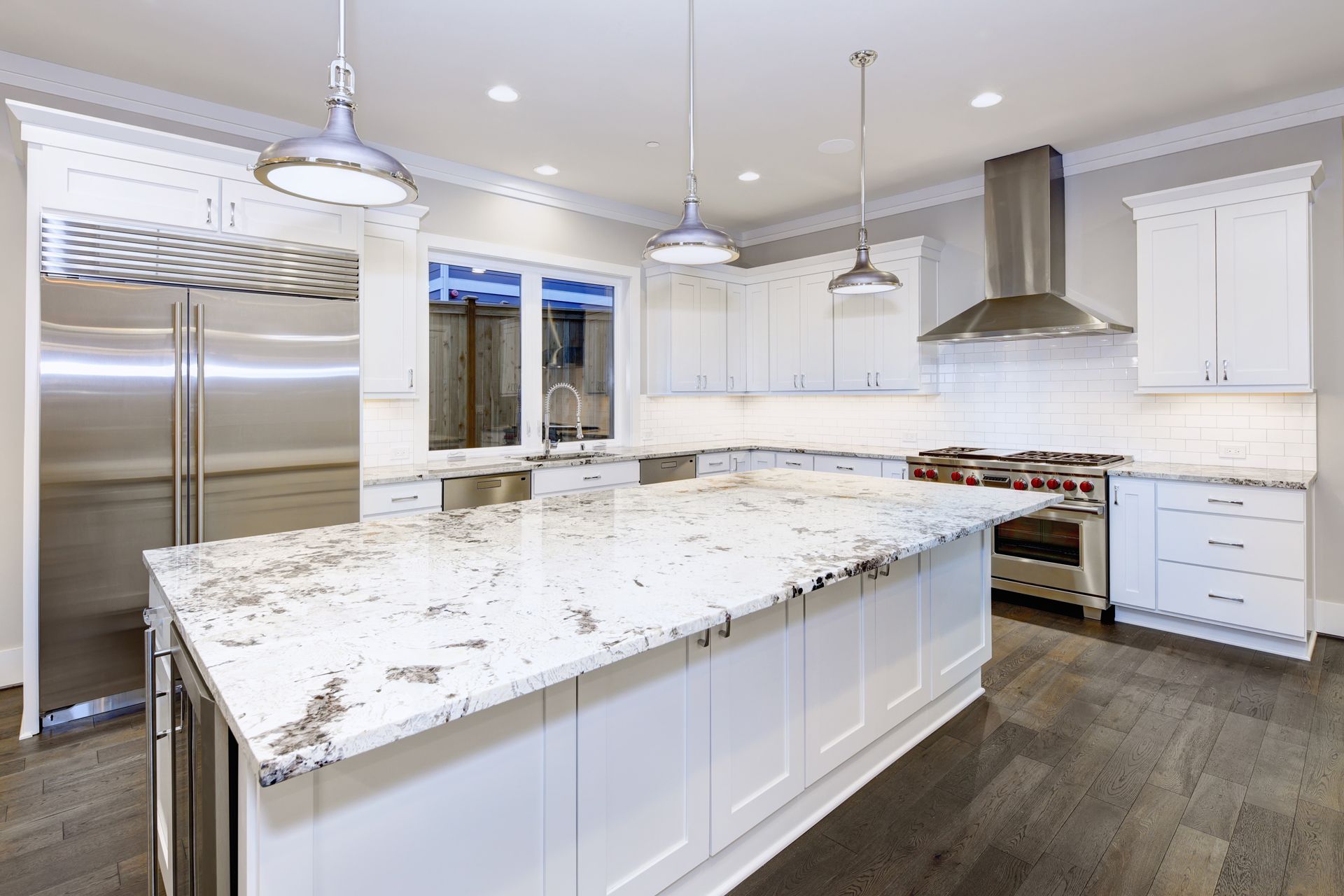 Bright modern kitchen with white cabinets, granite island, stainless steel appliances, and pendant lights