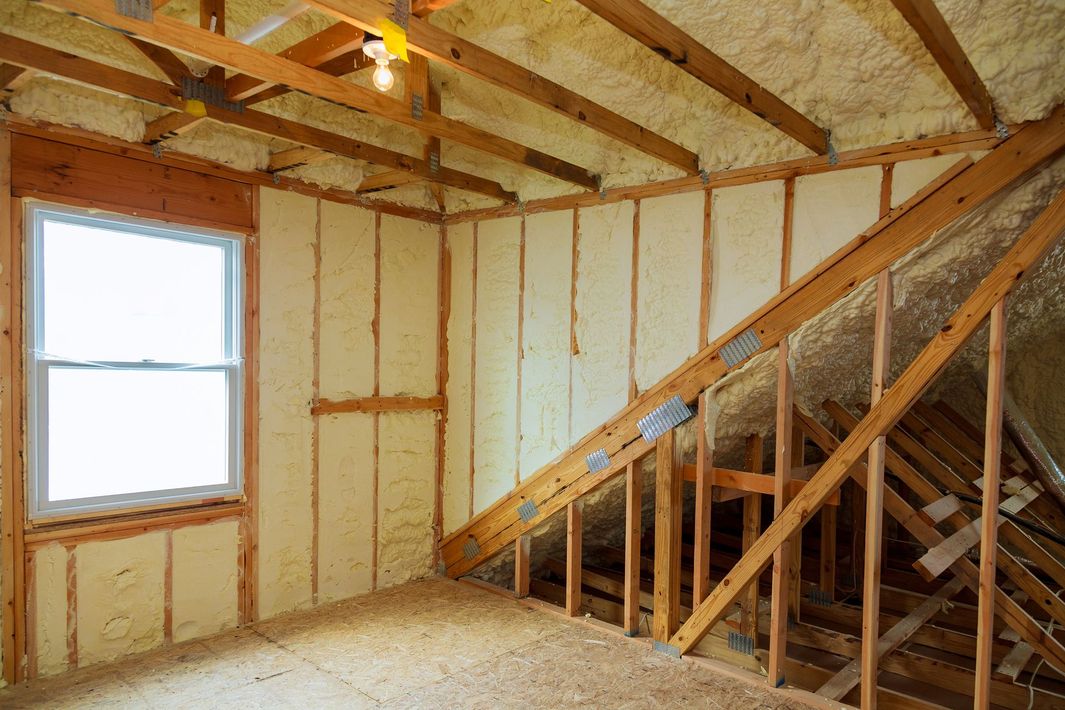 Unfinished attic room with exposed studs, insulation, a window, and a staircase under construction