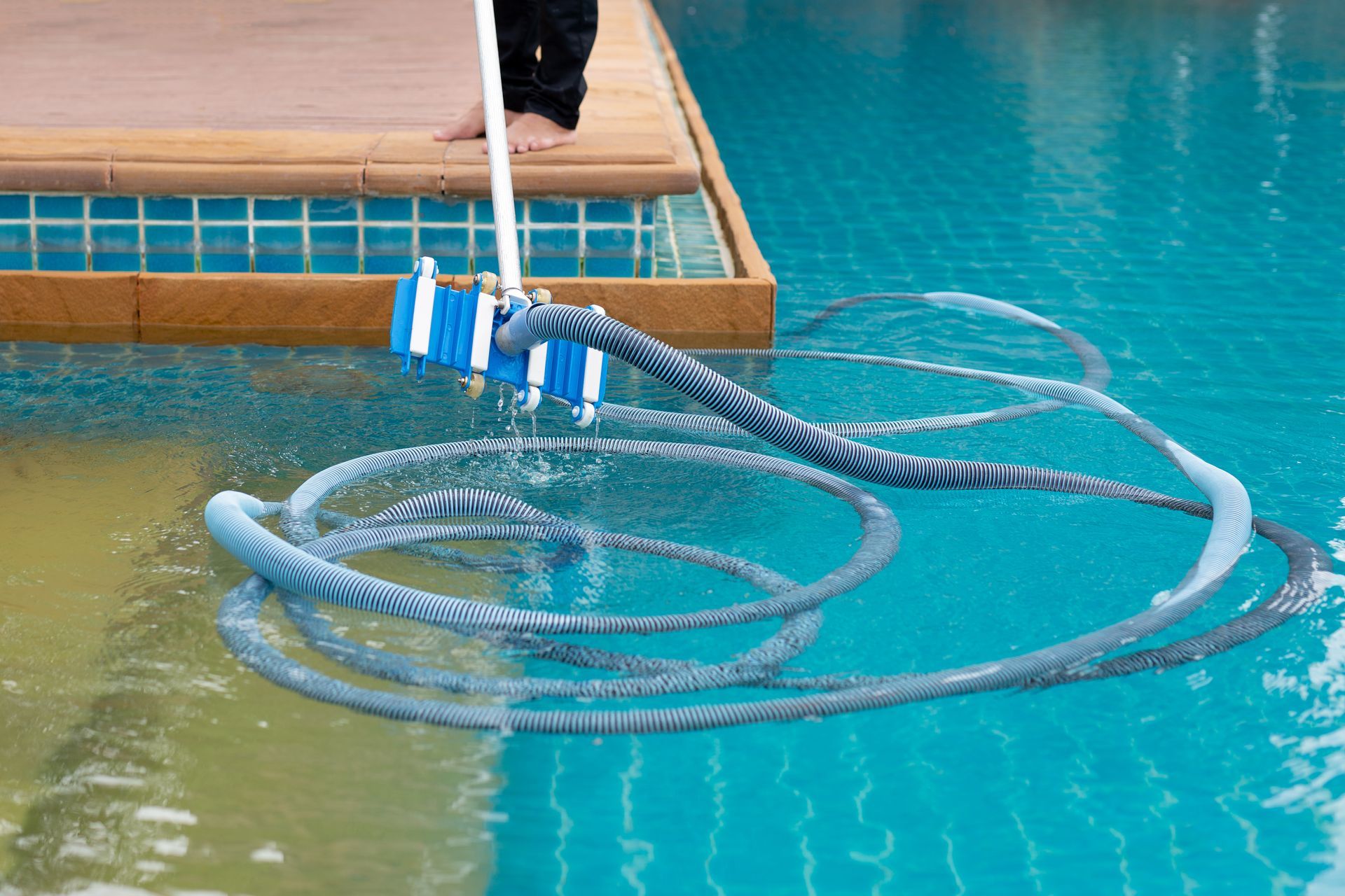 A person is cleaning a swimming pool with a broom and hose.