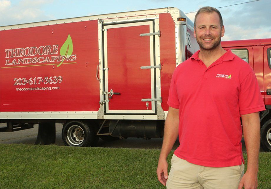 Scott from Theodore  in a red shirt stands in front of a red truck that says Theodore landscaping