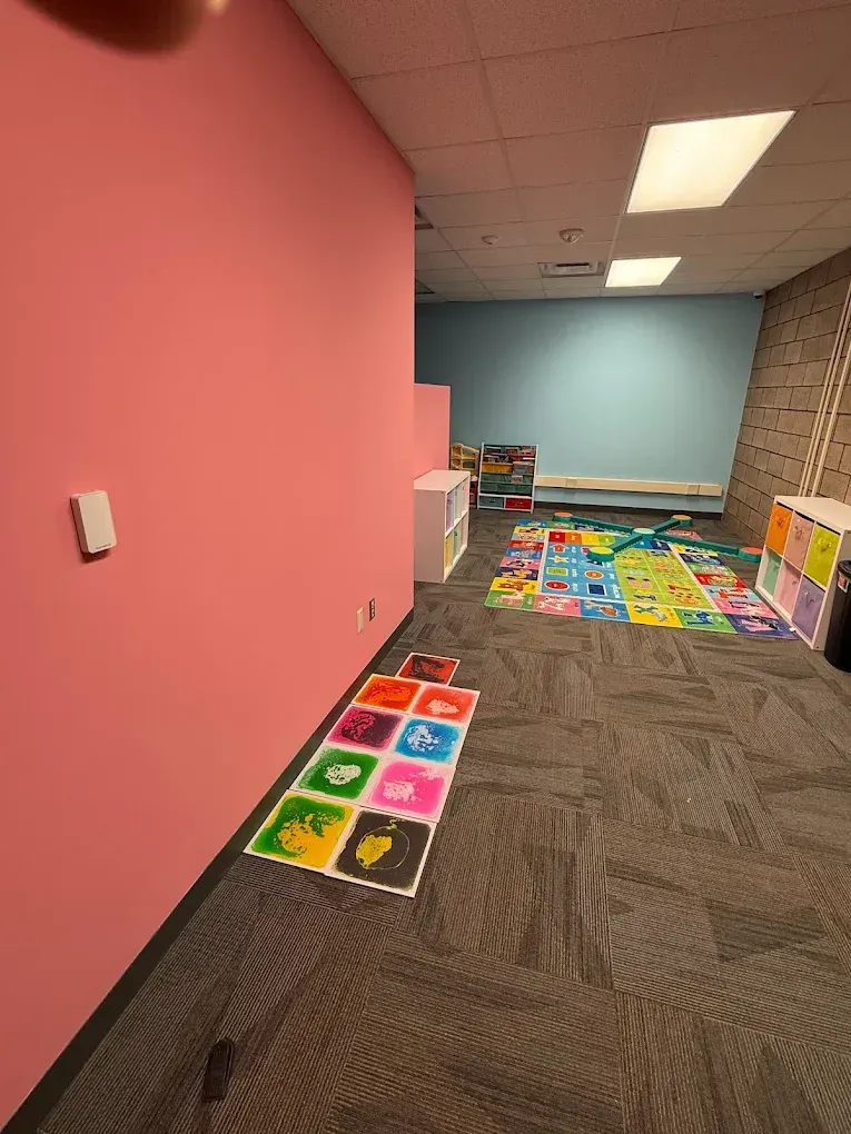 Playroom with pink and blue walls, colorful play mats, and storage shelves on gray carpet.