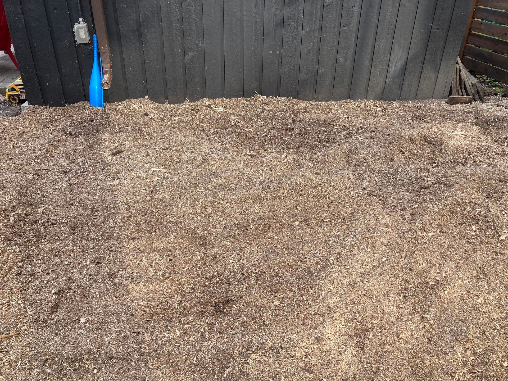 Pile of wood chips in front of a dark wooden fence.