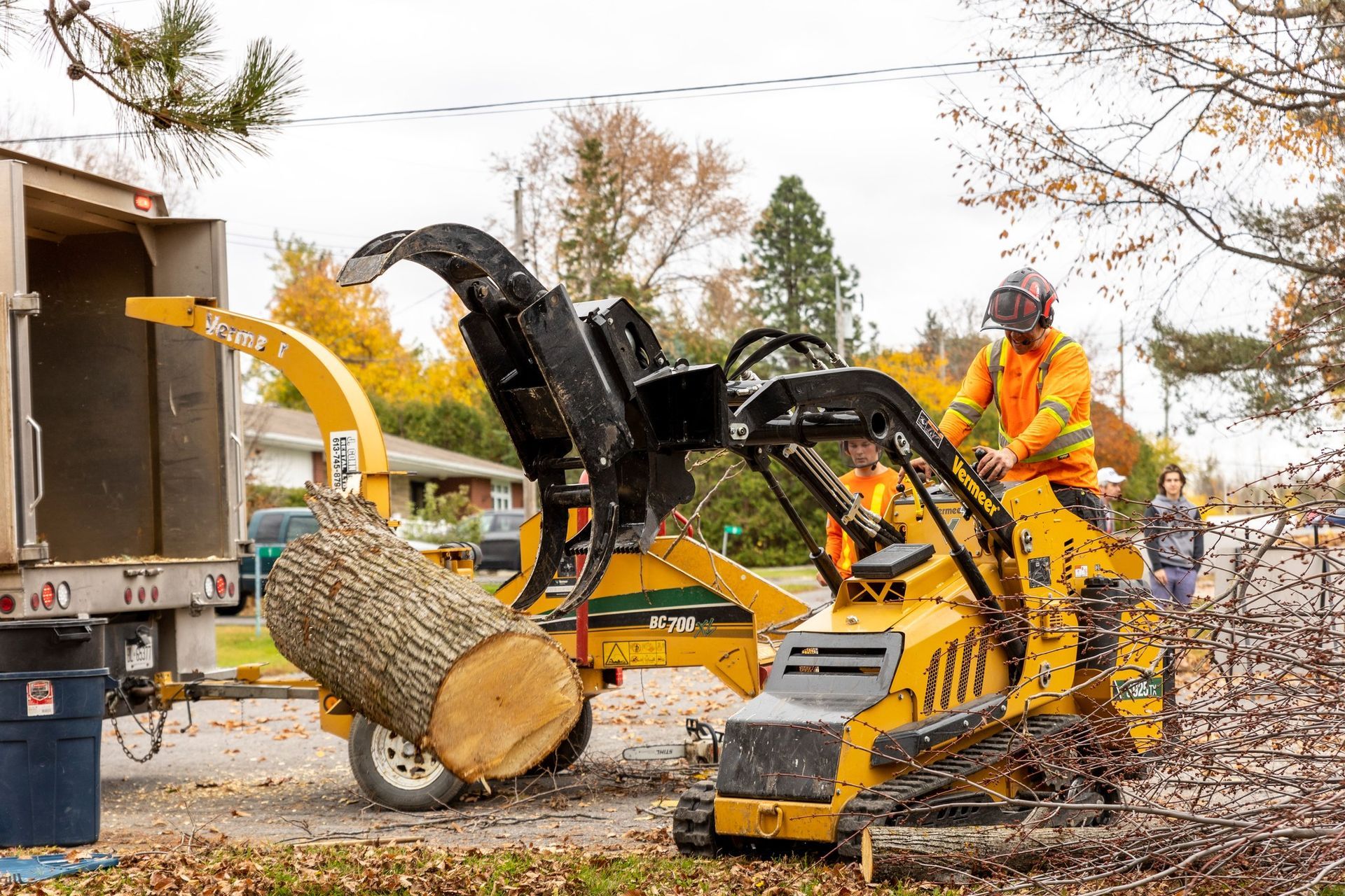A worker feeds a large log into a yellow wood chipper on a street.