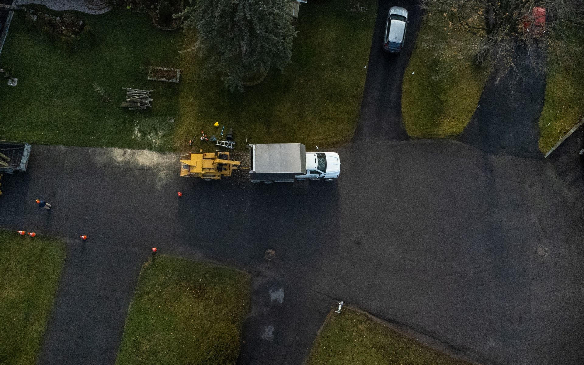 Overhead view of a truck towing a piece of yellow construction equipment, parked on a paved road near a green lawn.