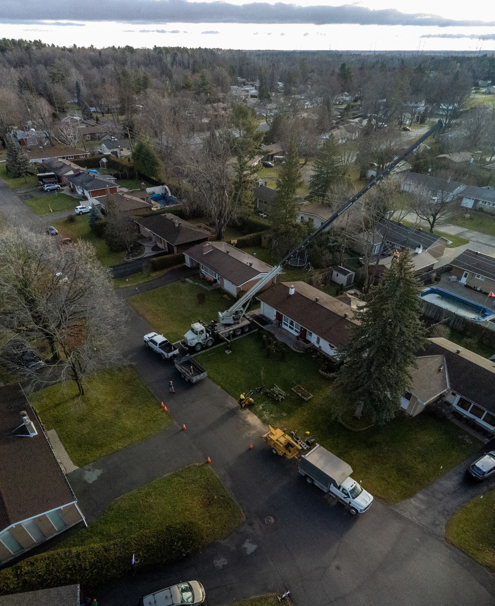 Aerial view: trucks and equipment servicing a row of houses. Trees in the background.