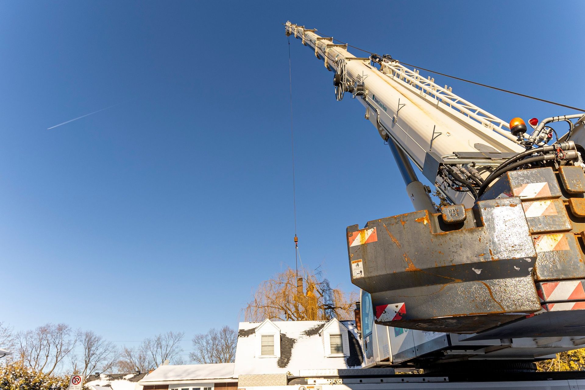 A large crane lifting something over a house on a sunny day.