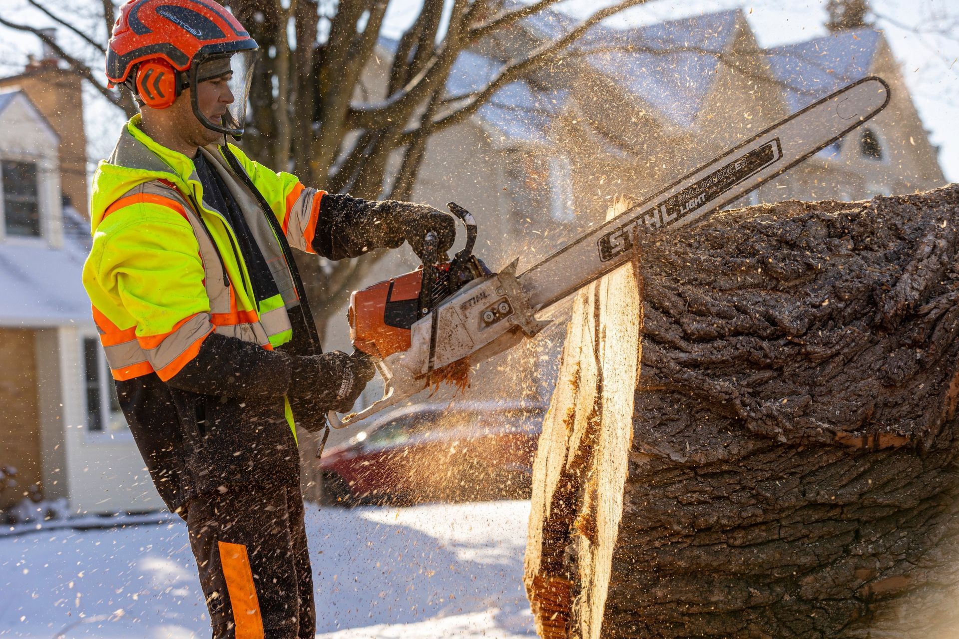 Arborist in safety gear cutting a tree trunk with a chainsaw outdoors in winter.