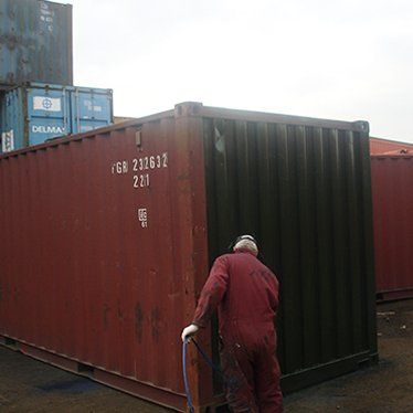 Man spraying black paint on red shipping container.