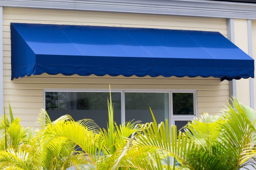 Blue Awning Over White Aluminium Frame Window Of Shop — Get Awnings in Mollymook, NSW