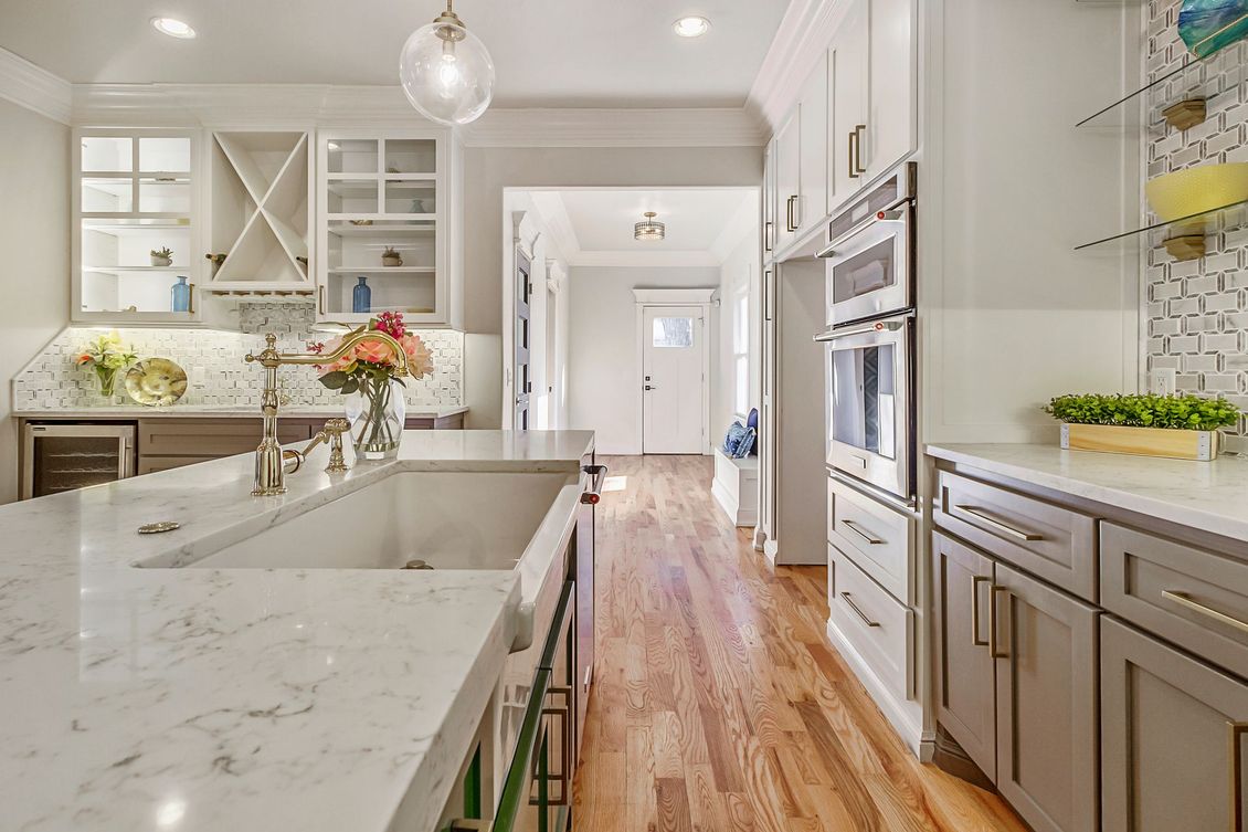 Bright kitchen with white and gray cabinets, marble countertops, and wooden floors.