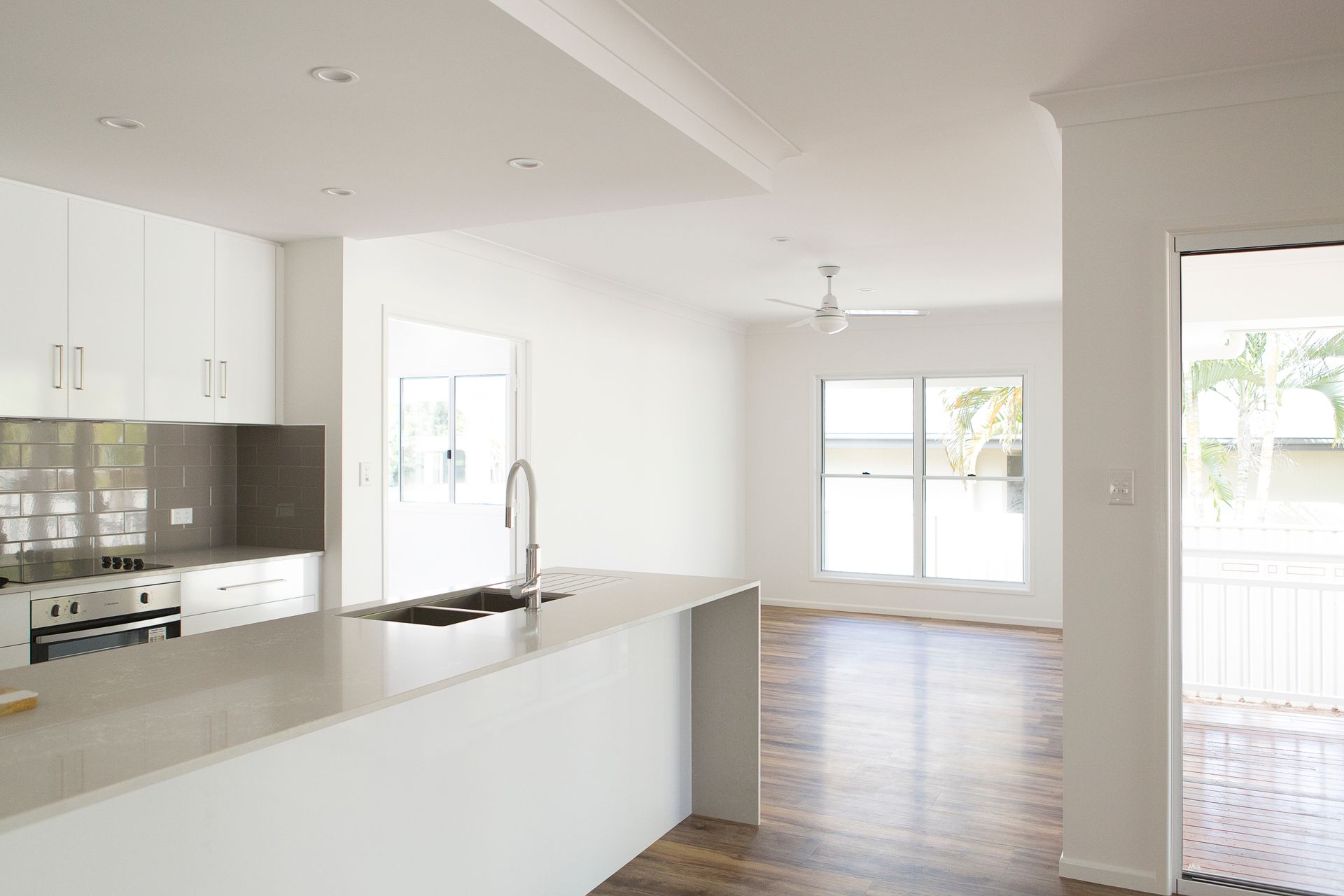 Modern, white kitchen with island, sink, and open layout to living area.