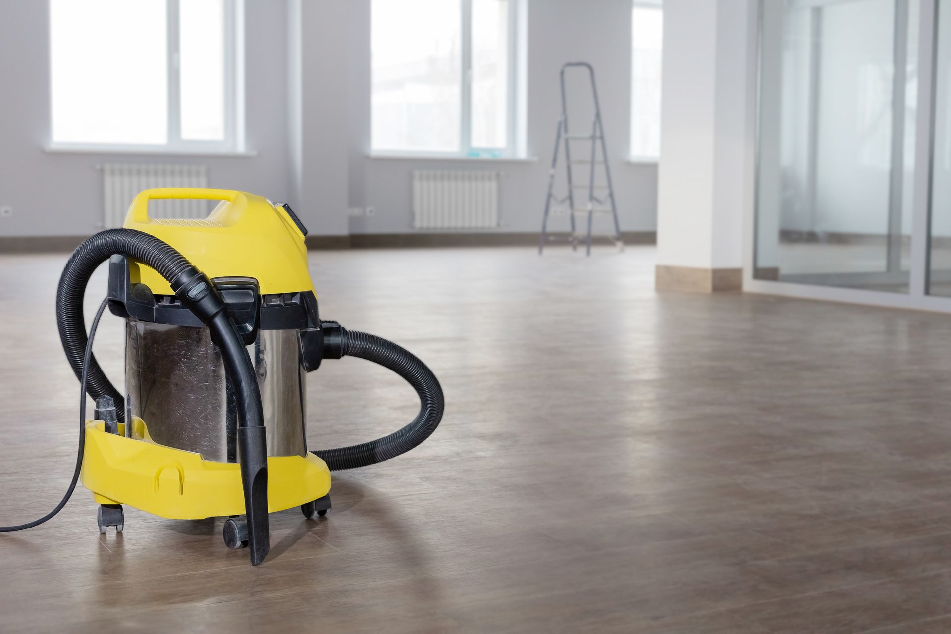 Yellow and stainless steel vacuum cleaner in an empty, recently cleaned room with a ladder.
