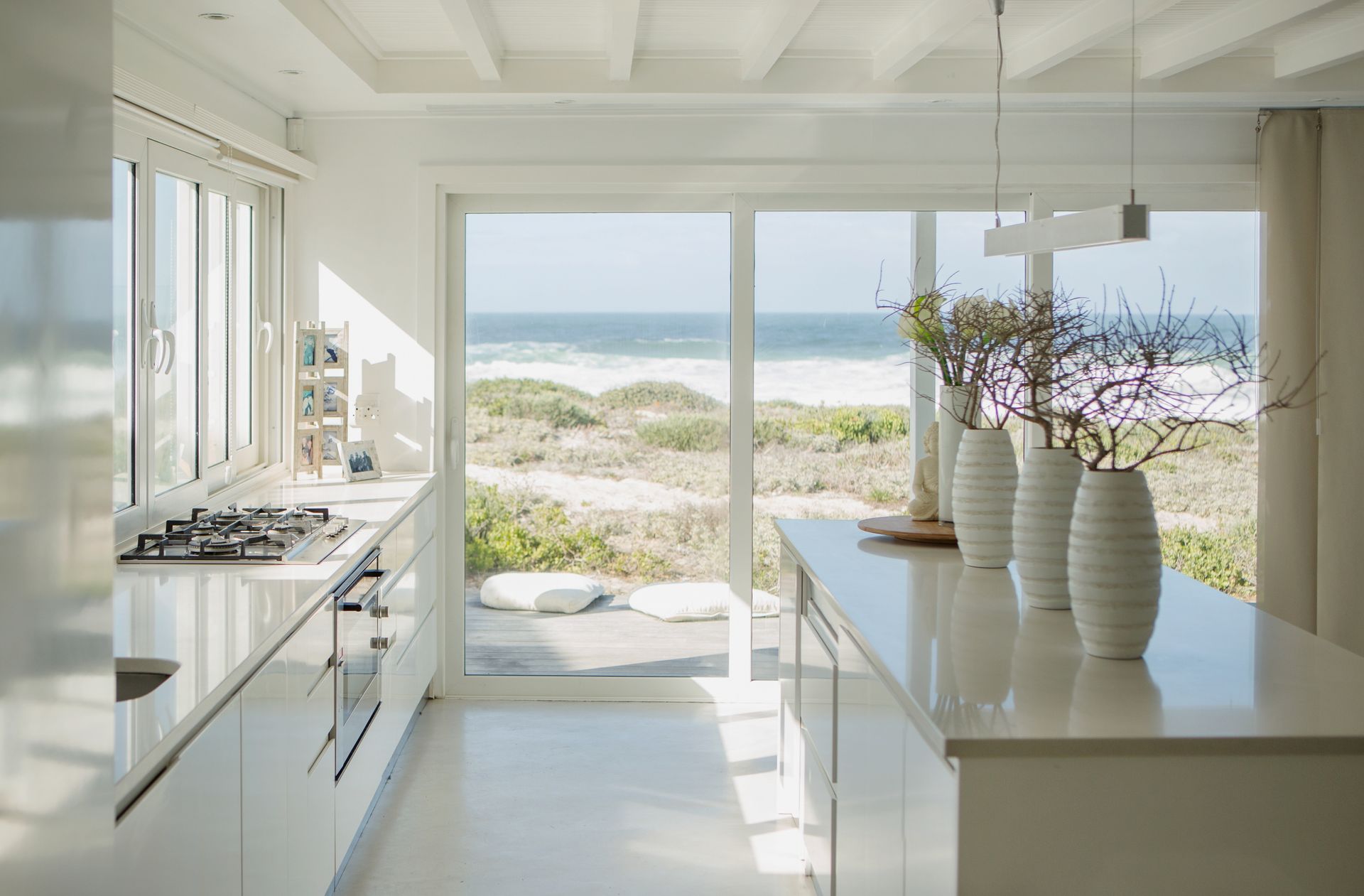 Modern white kitchen with ocean view, countertops, island with vases, and large windows.