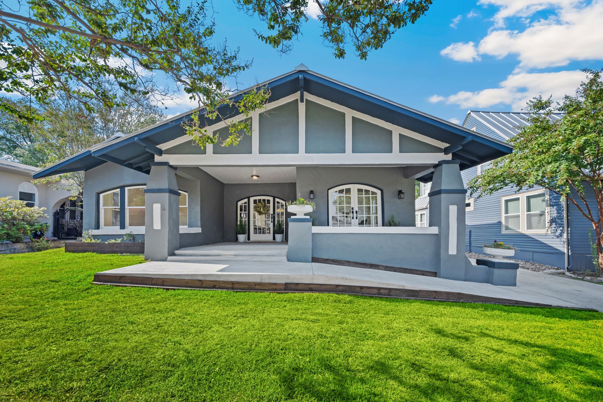 Gray Craftsman-style house with a porch, green lawn, and blue sky.