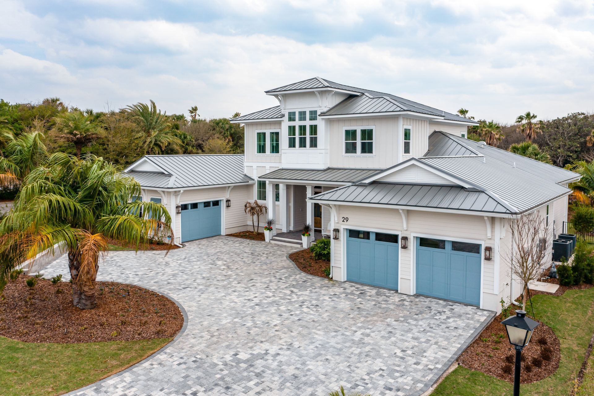 White two-story house with blue garage doors, a gray stone driveway, and a green lawn.