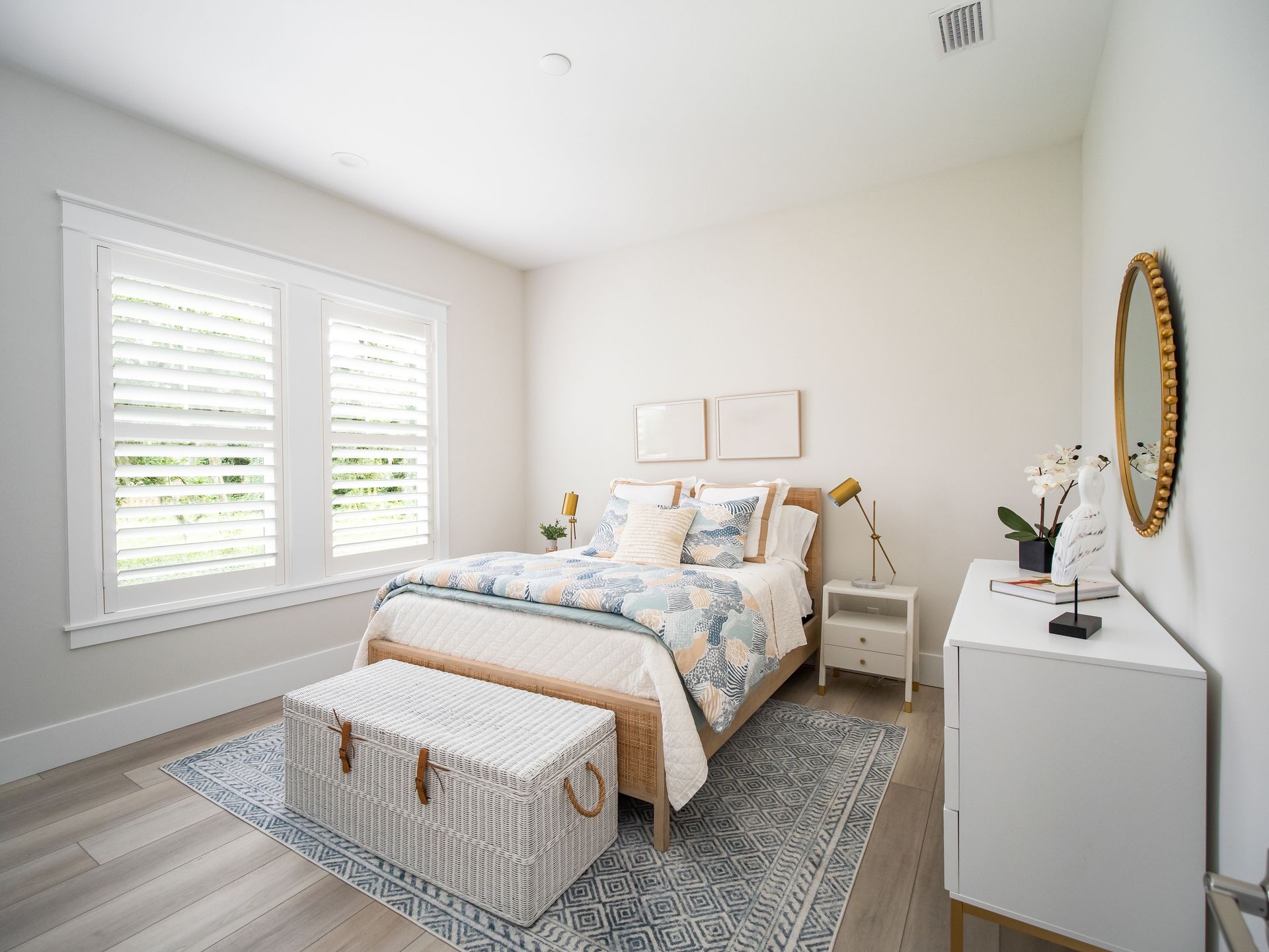 Bedroom with bed, dresser, window with shutters, and trunk, neutral tones with blue accents.