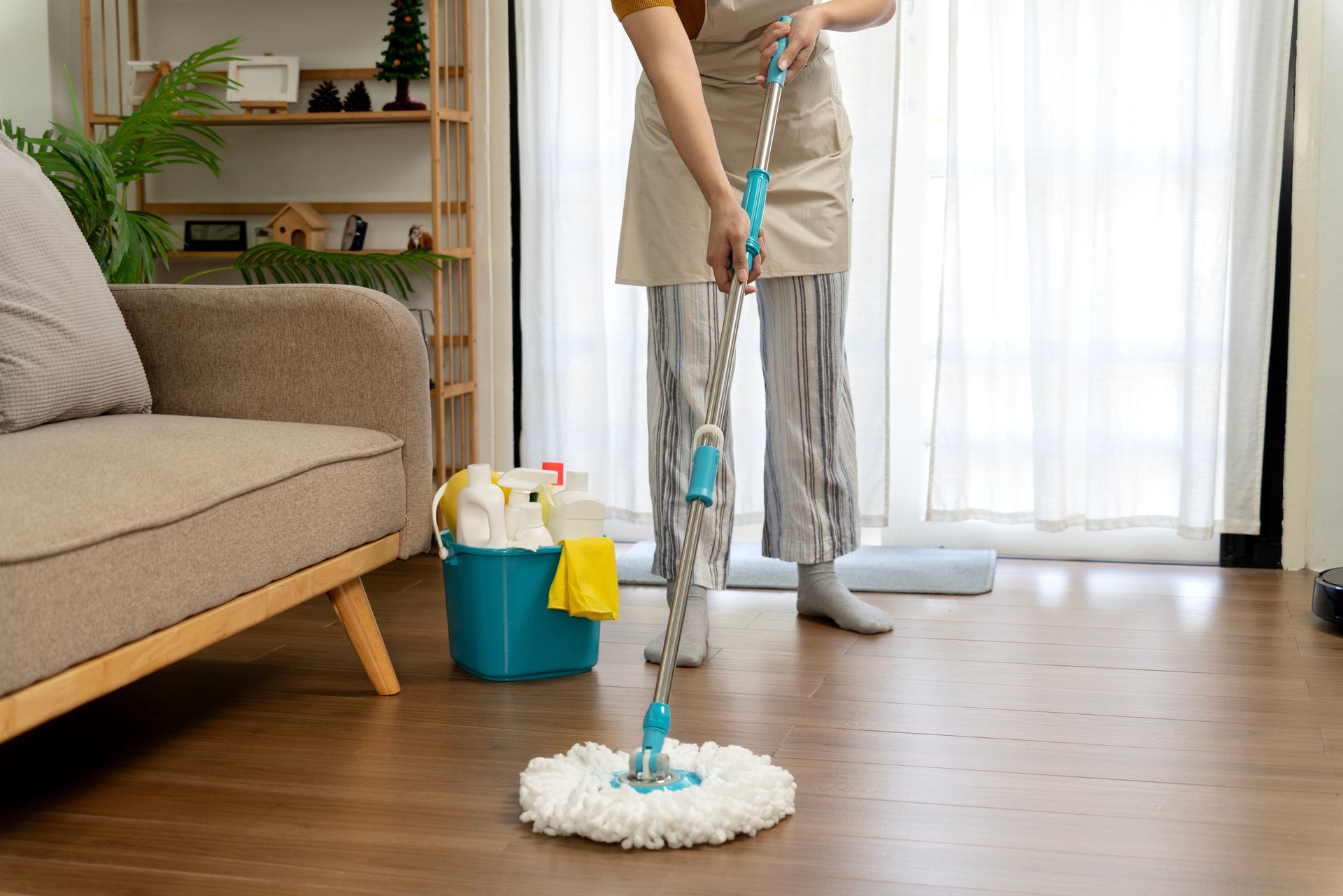 Cardboard boxes, cleaning supplies, and mop in room with wooden floor and white door.