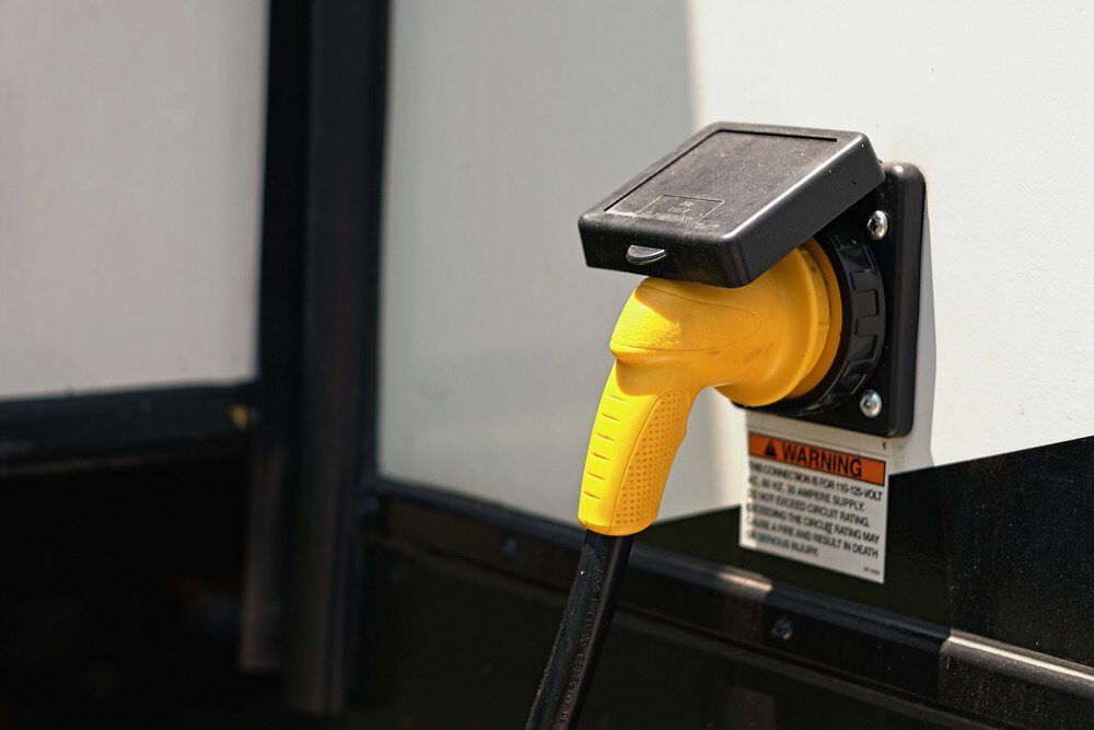 Yellow Rv Power Cord Plugged Into a Port on a White Exterior Wall — Direct Current Solutions in Mareeba, QLD