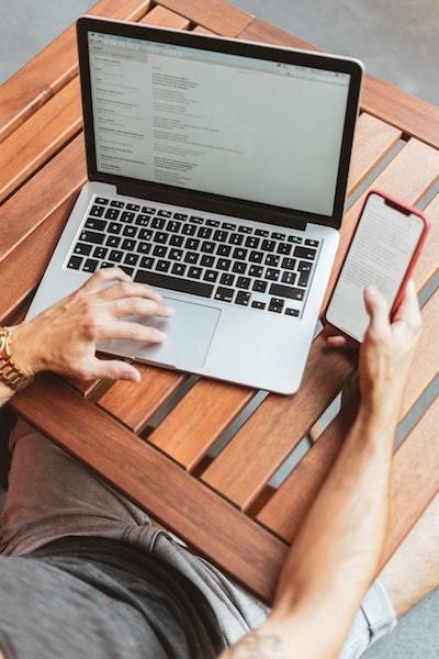 Vista aérea de una persona usando una computadora portátil y un teléfono inteligente mientras está sentada en una mesa de madera con listones.