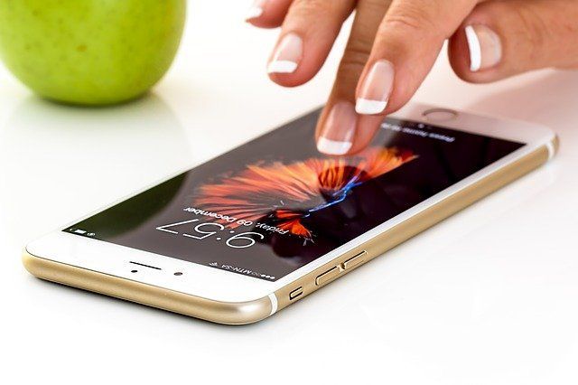 La mano de una persona toca la pantalla de un teléfono inteligente dorado que muestra un gráfico abstracto y colorido junto a una manzana verde.