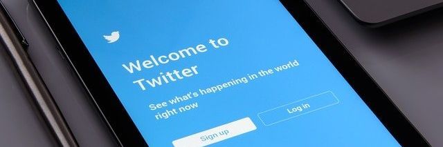 La pantalla de un teléfono inteligente muestra la página de bienvenida de Twitter con un fondo azul, el logotipo y los botones de registro e inicio de sesión.