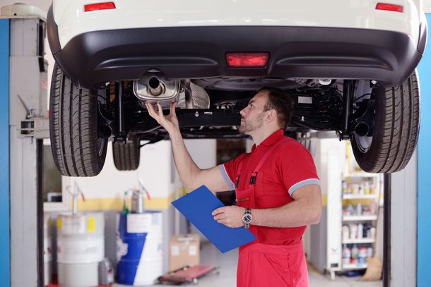 A man is working on the exhaust pipe of a car in a garage.