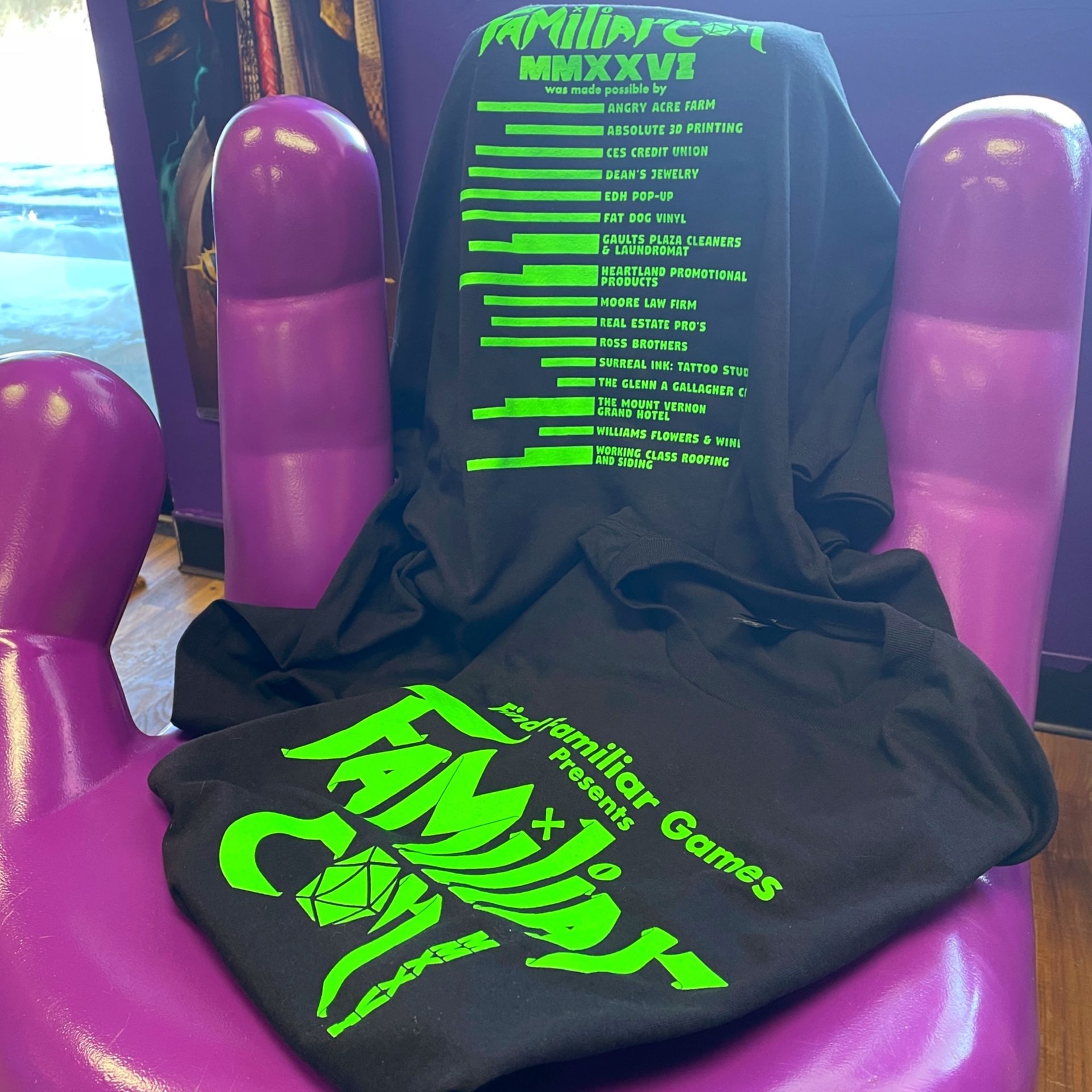 Image of Familiar Con MMXXVI t-shirt front and back draped over a large purple hand chair.