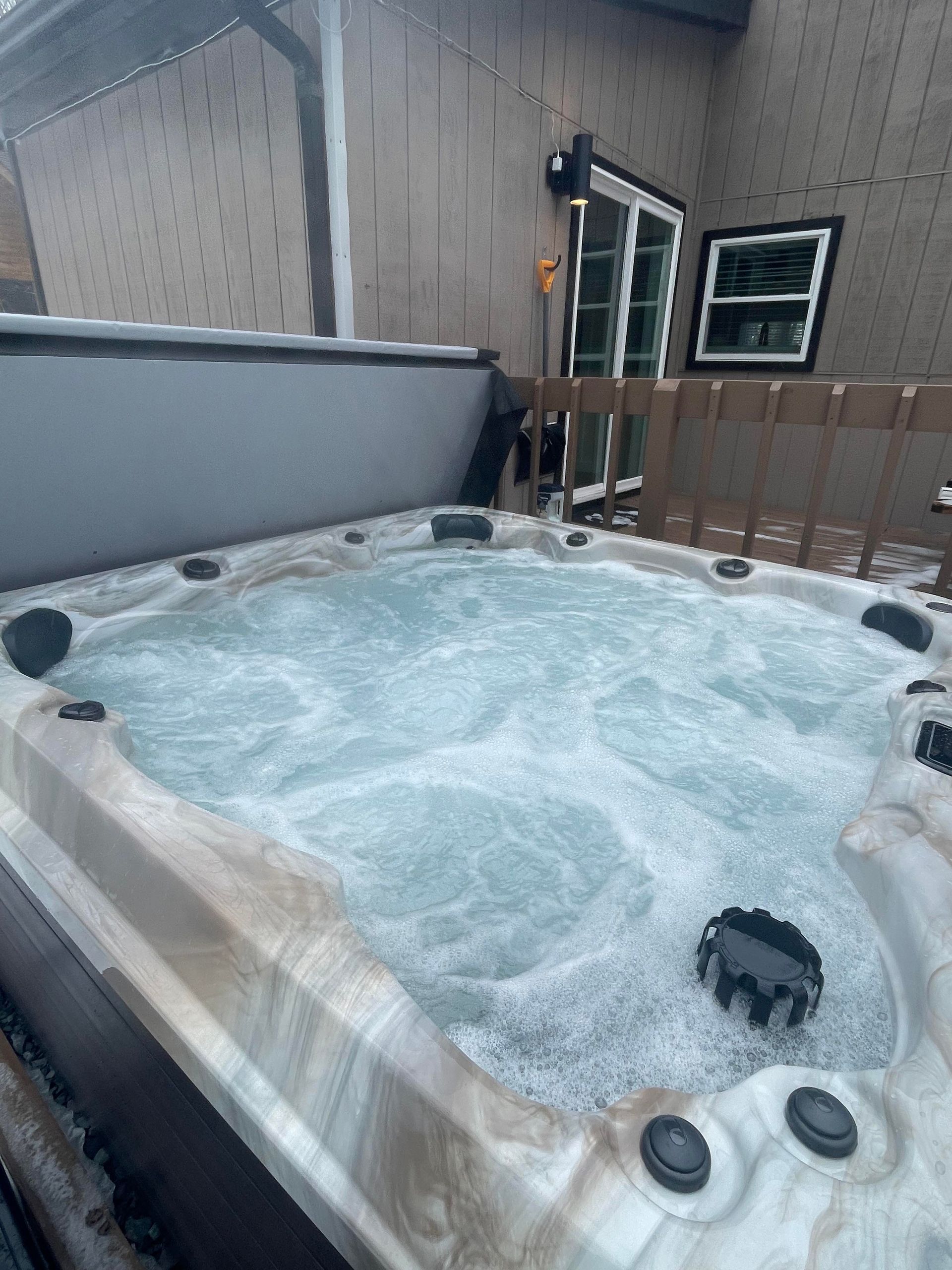 A hot tub is sitting on a deck next to a house.