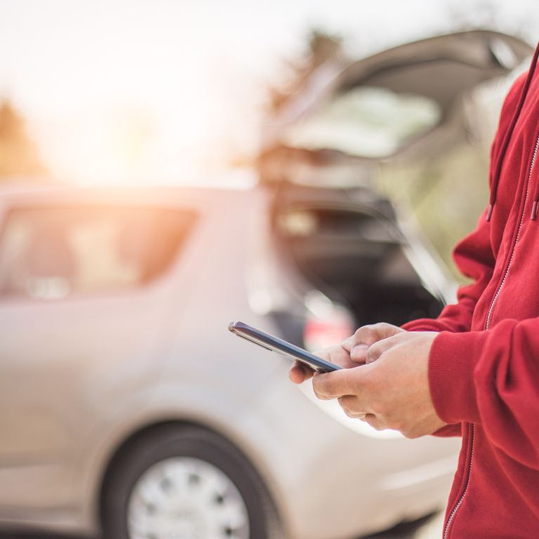 A person is holding a cell phone in front of a car.
