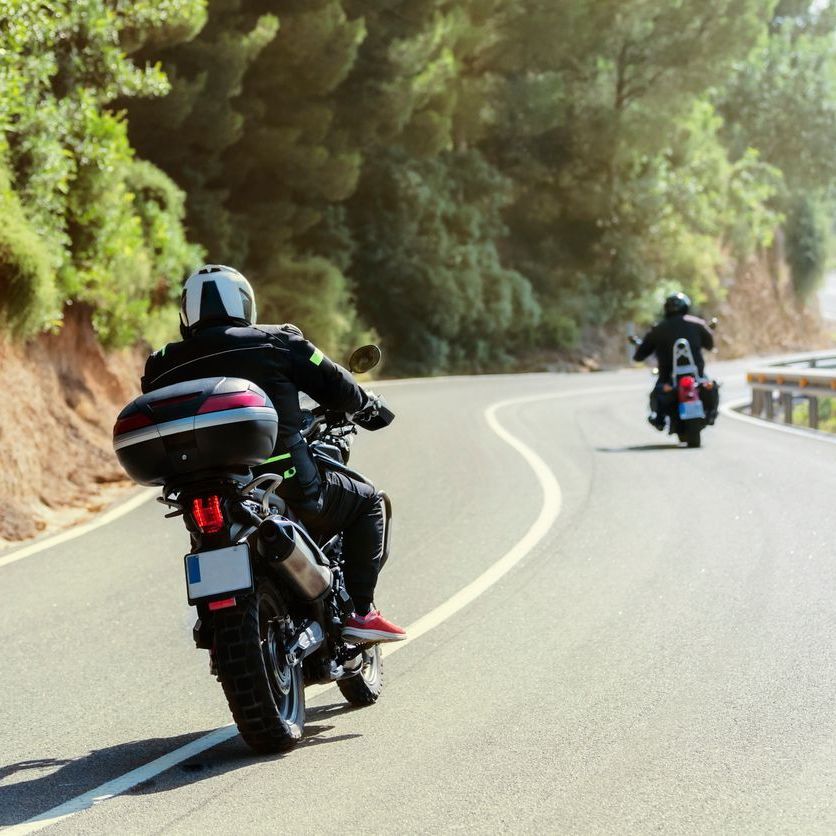 Two people are riding motorcycles down a curvy road
