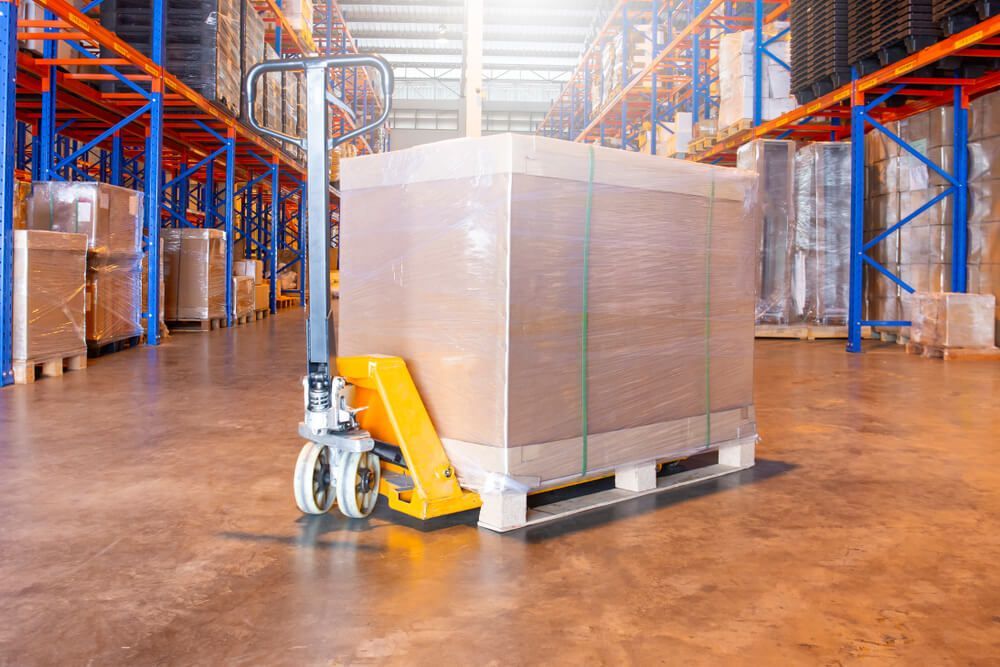 A Pallet Truck Is Carrying A Large Box In A Warehouse — Uplift Removals in Burdell, QLD