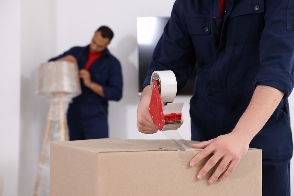 Movers Packing Boxes With Tape in a Bright Room — Uplift Removals in Brisbane, QLD