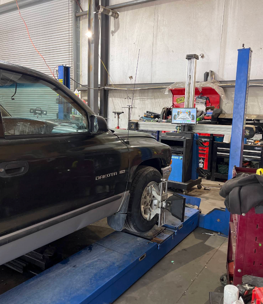 Black SUV on a lift inside an auto repair shop, with a wheel removed during service. | Momax Wheels and Auto LLC
