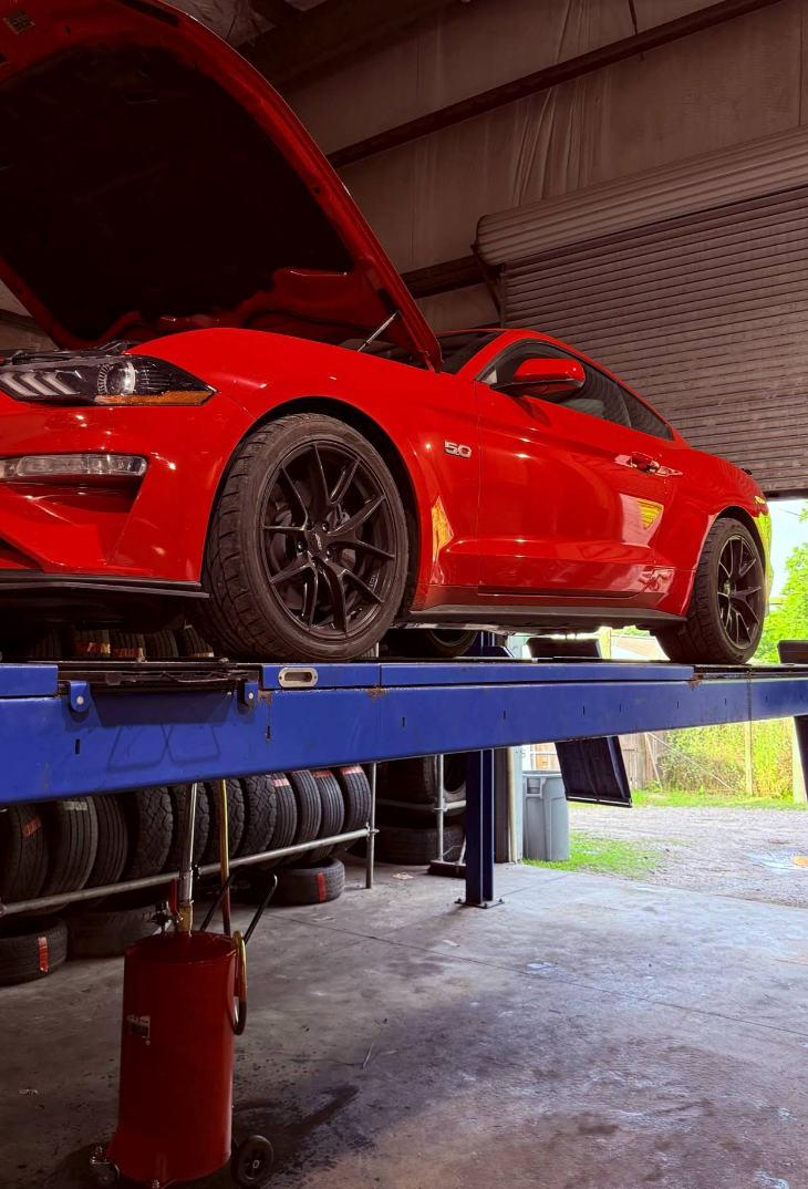 Red sports car lifted on a blue hydraulic car lift in an auto repair garage | Momax Wheels and Auto LLC