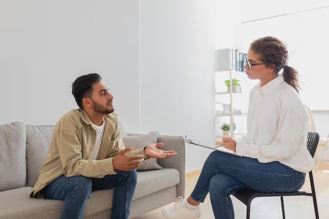 Two people talking in a bright living room, seated on a couch and chair