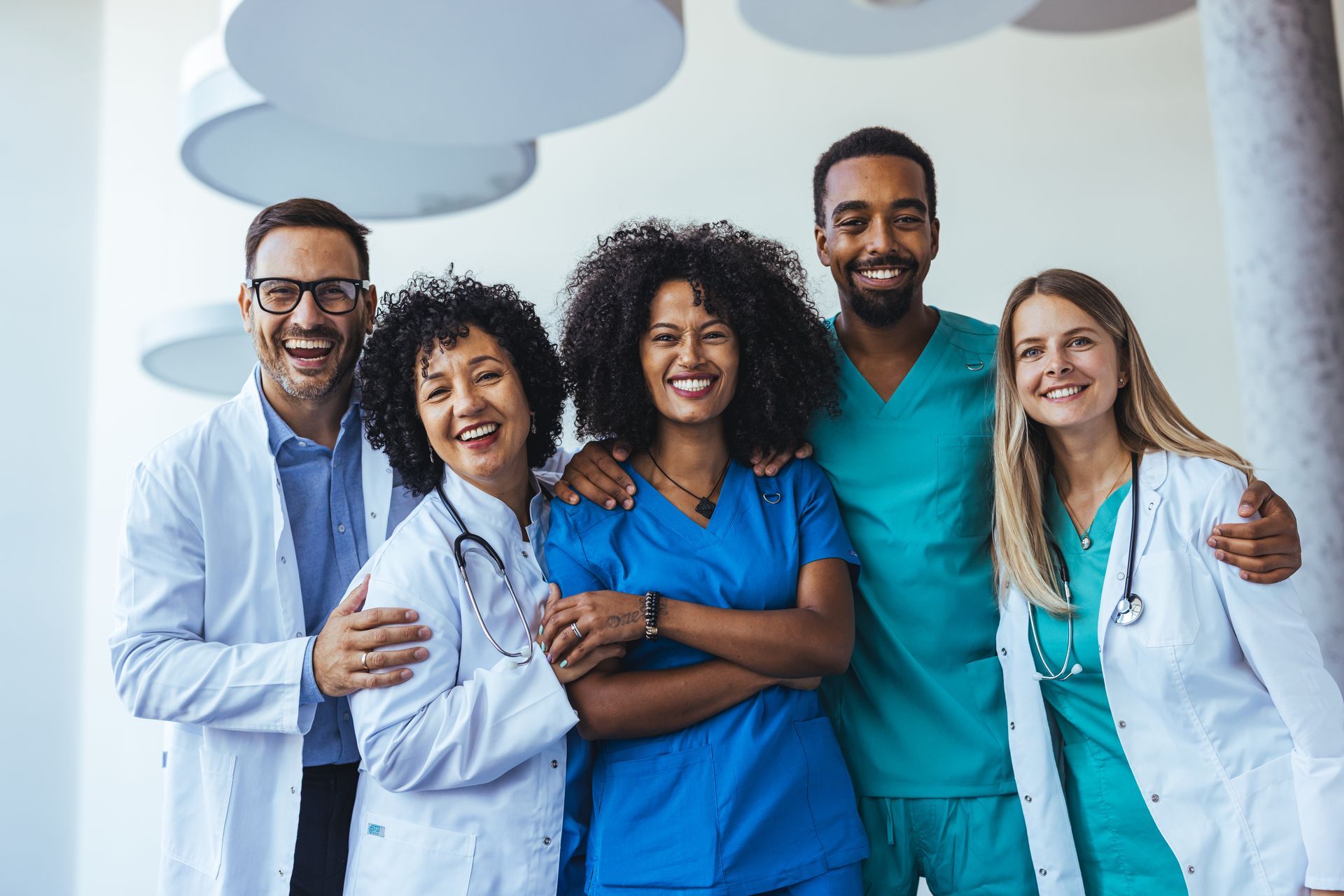 Medical team smiling, diverse group in scrubs and lab coats, indoors.