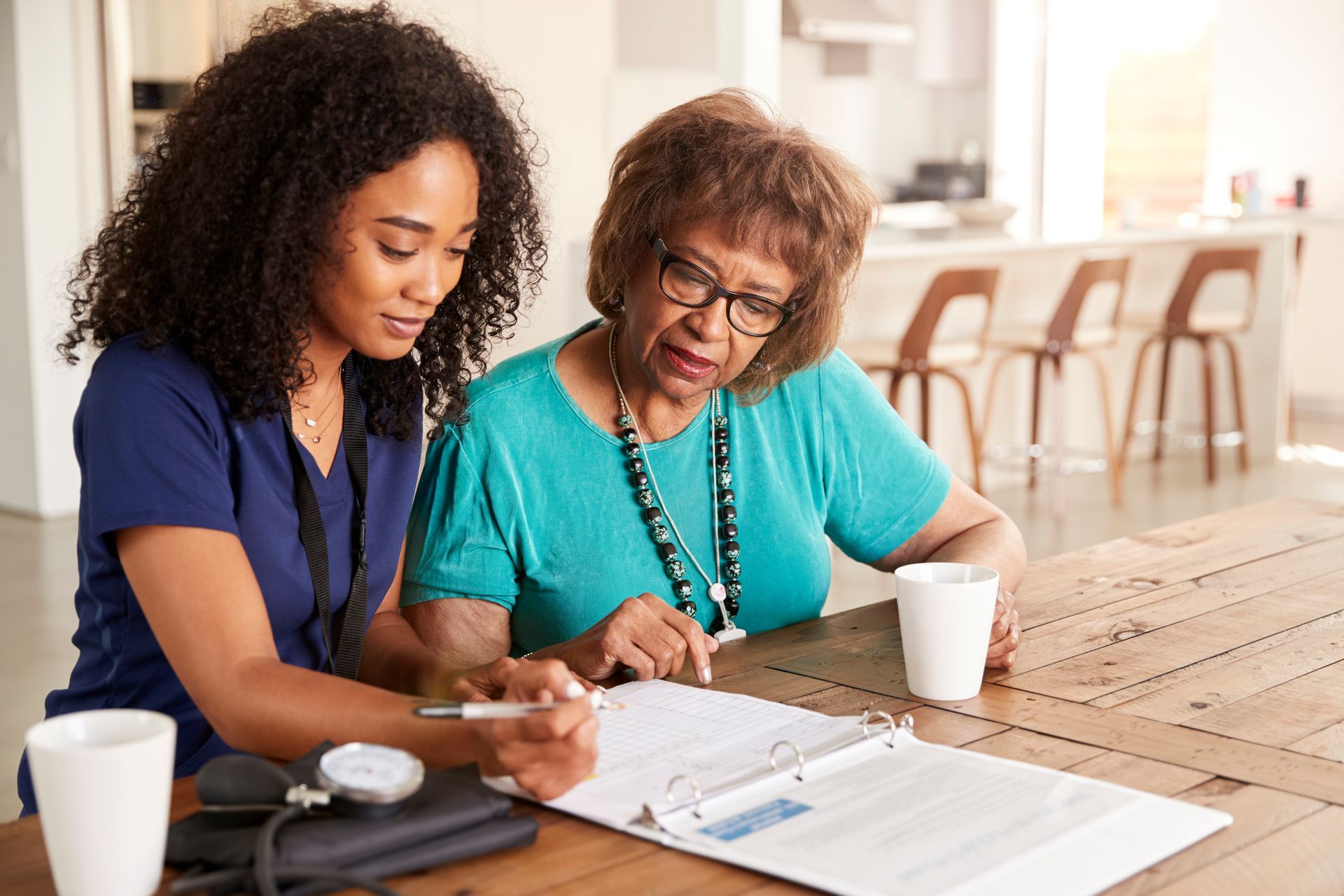 Caregiver and older adult reviewing paperwork at a table; interior setting.