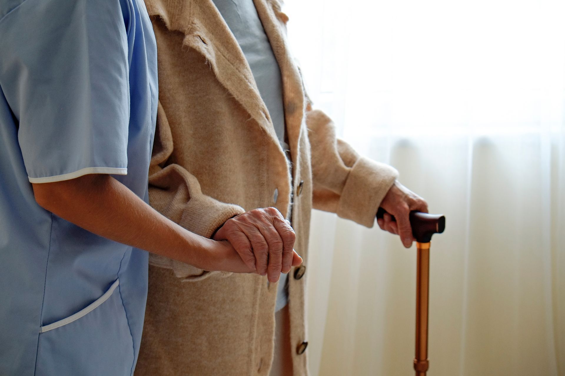 Caregiver assisting a person with a cane to walk indoors.