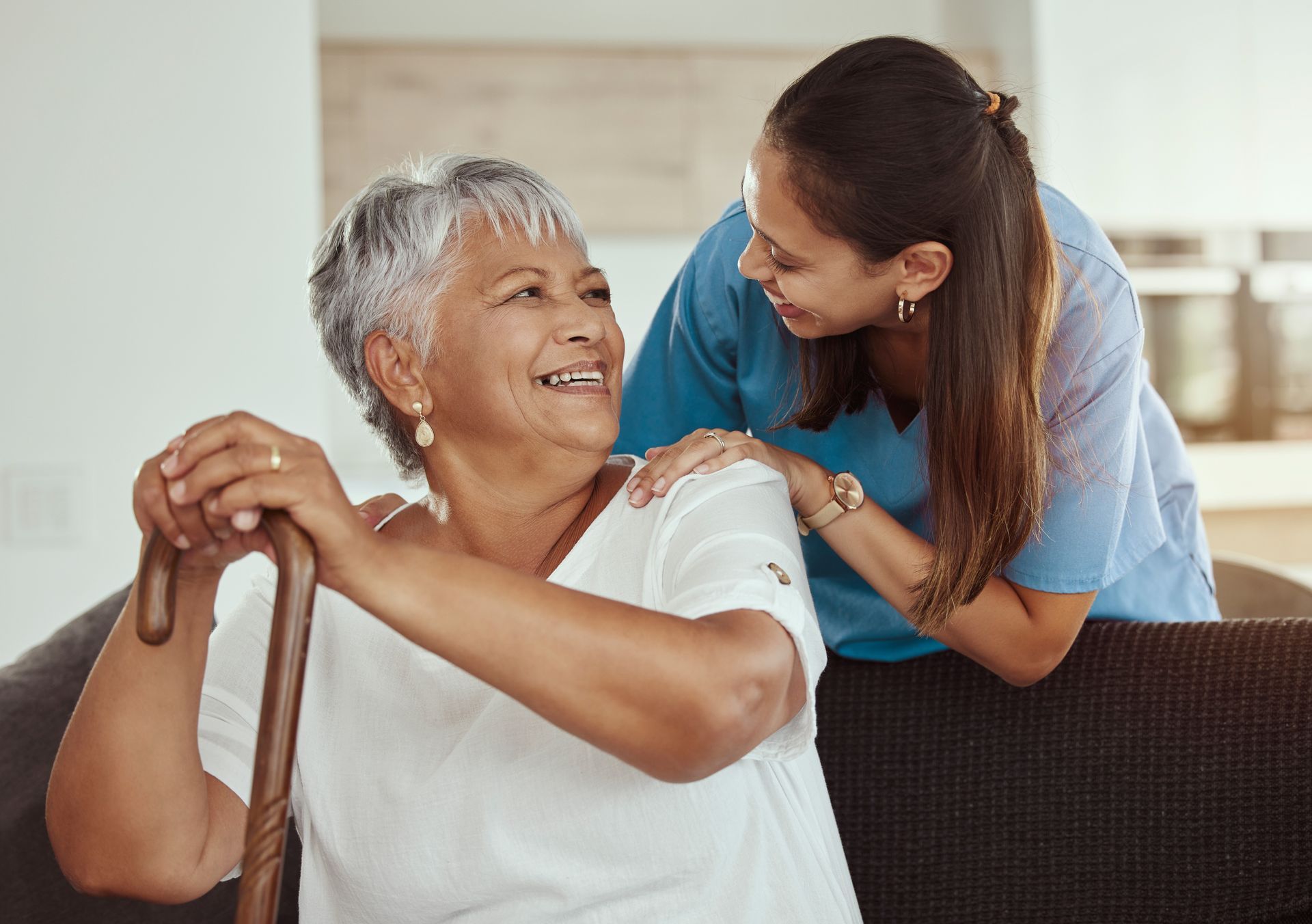 Woman with cane smiles at healthcare worker in home setting.