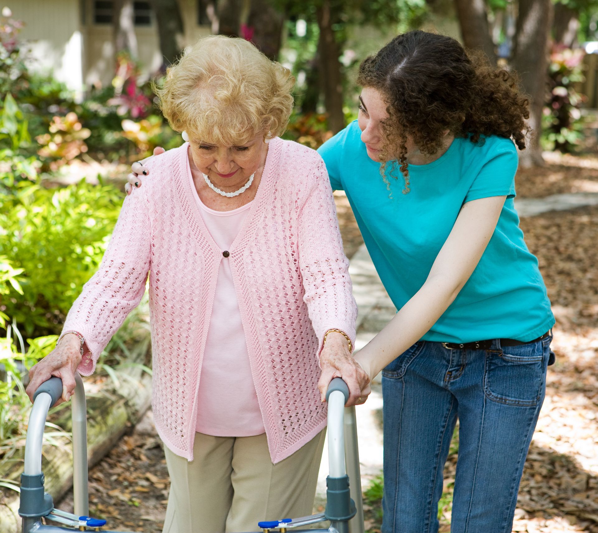 Woman using a walker assisted by a person in a turquoise shirt outdoors.
