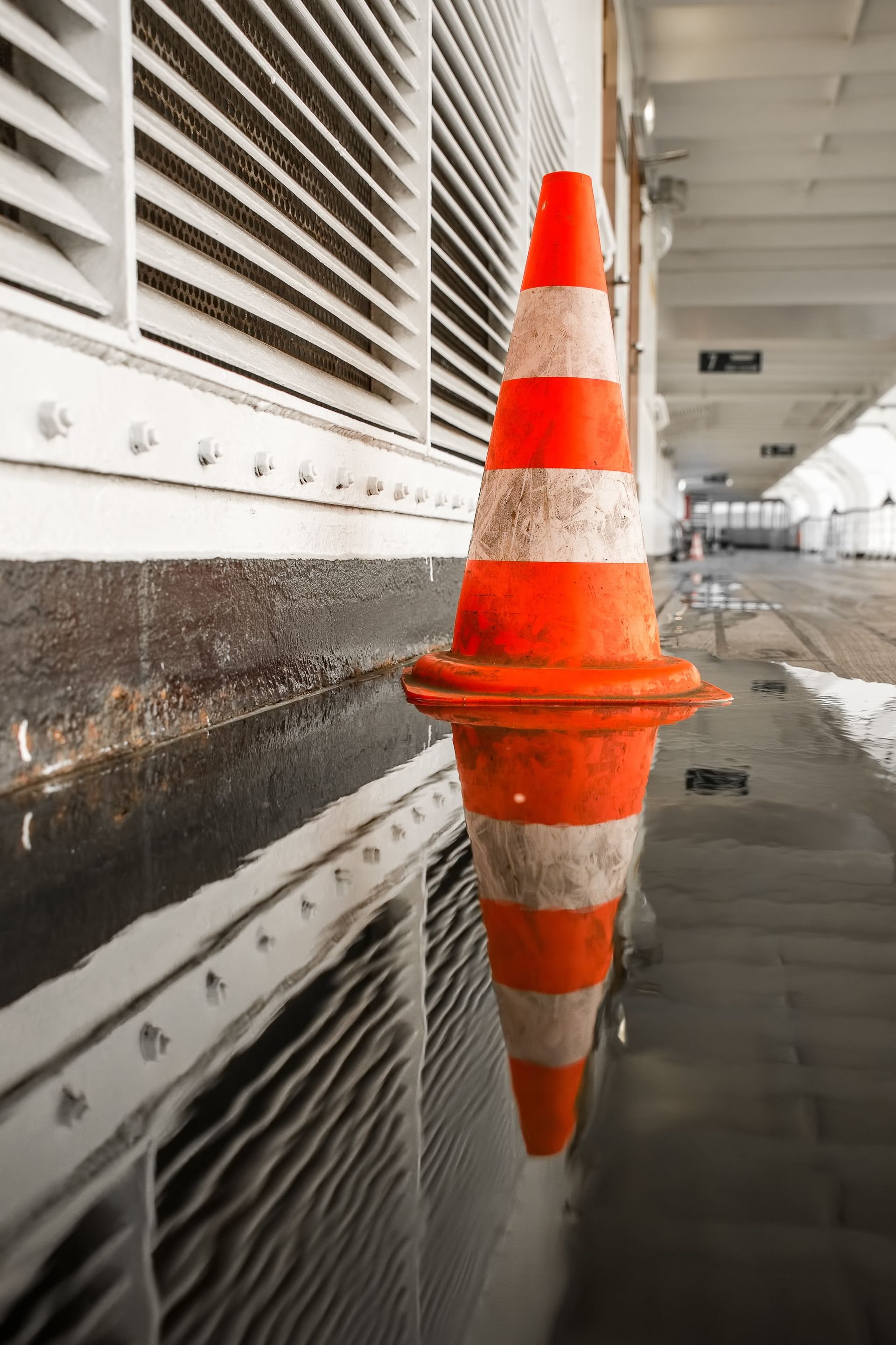 Um cone de trânsito laranja e branco é refletido em uma poça d'água.